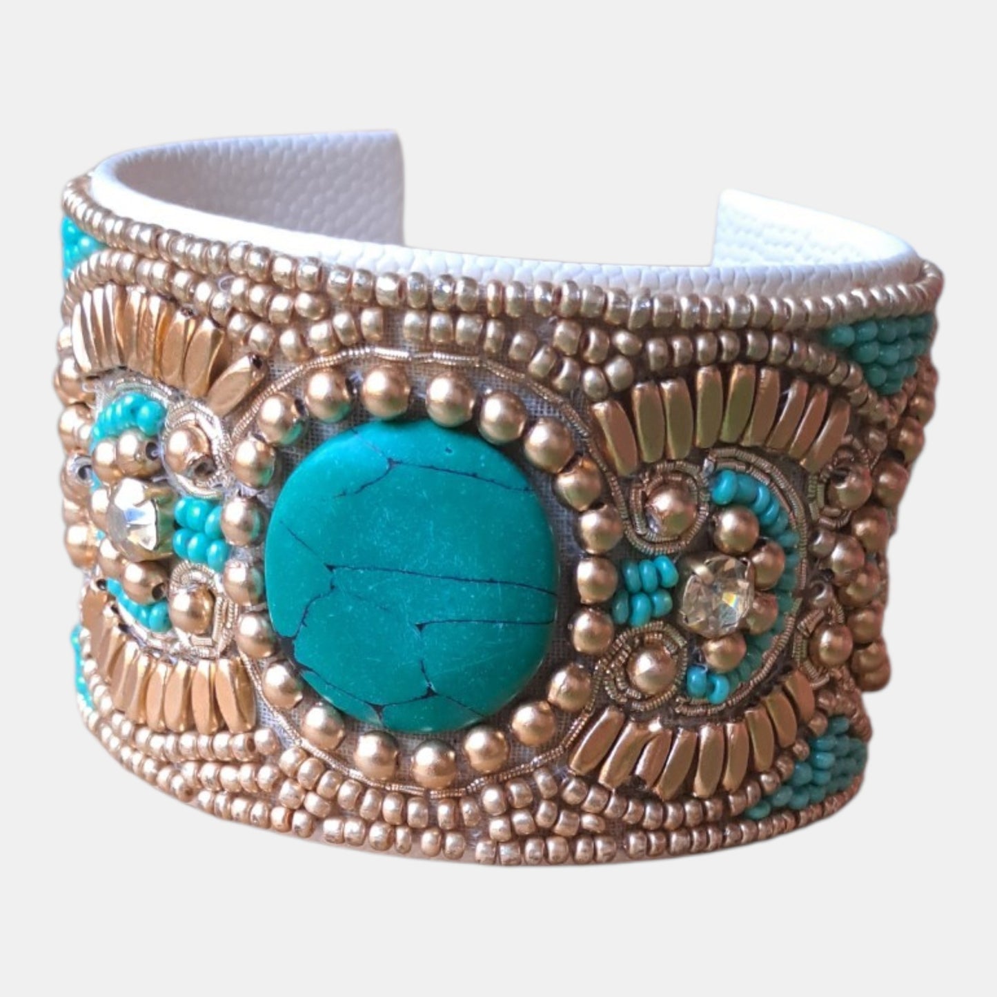 A wide cuff bracelet featuring a large round turquoise stone in the center, surrounded by intricate gold-toned beadwork, metallic accents, and smaller turquoise details, Measurements: 4,5cm wide, 18cm circumference