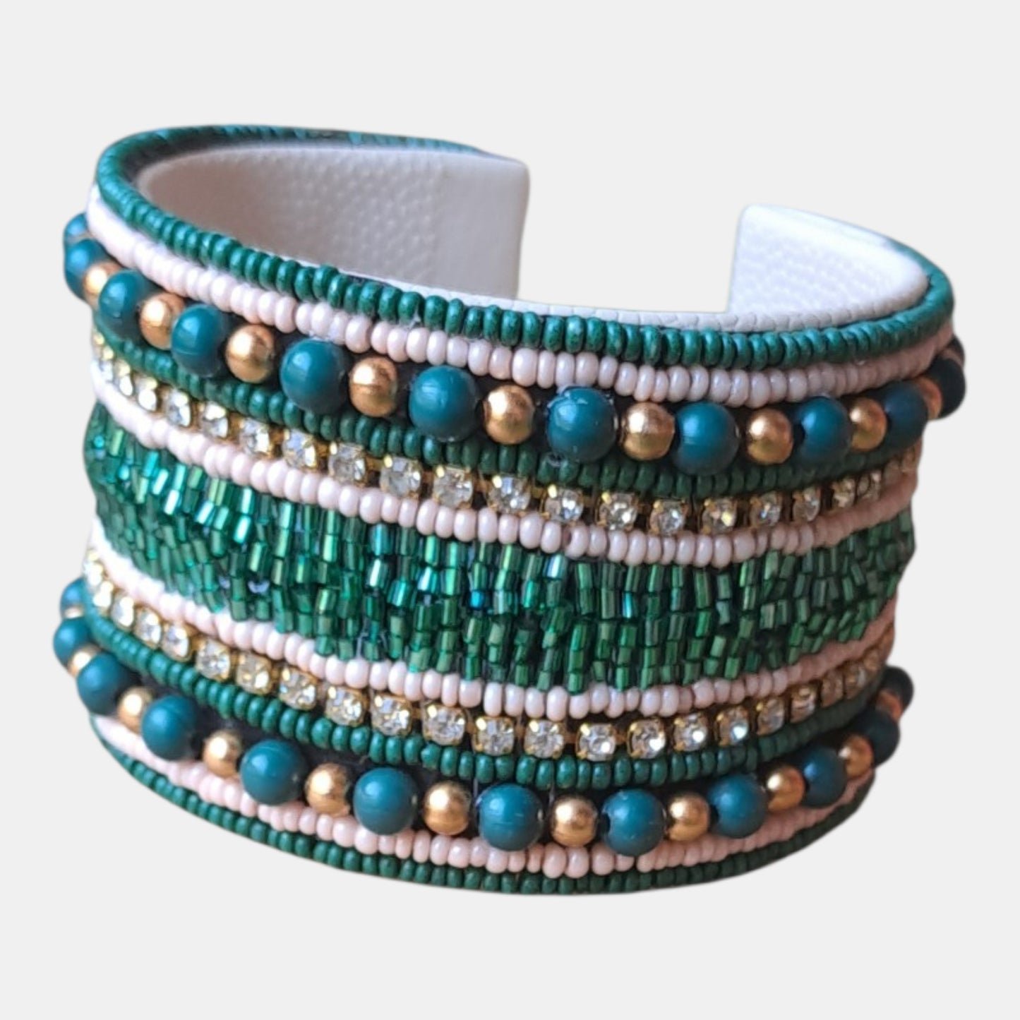 A multi-strand beaded cuff bracelet featuring horizontal bands of green seed beads, white beads, teal beads, metallic gold beads, and clear rhinestones,Measurements: 4,5cm wide, 18cm circumference