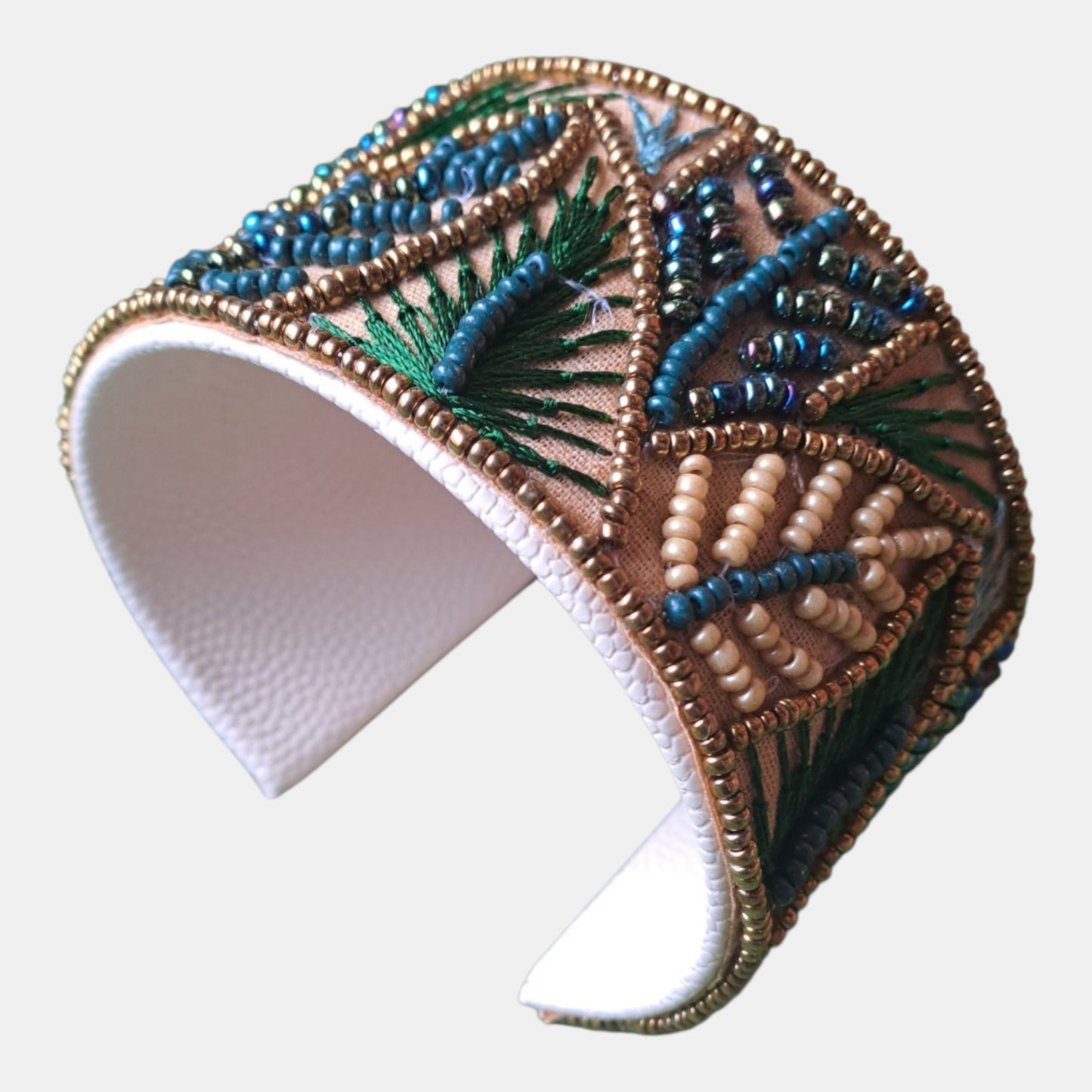 A wide cuff bracelet with intricate beaded and embroidered patterns in blue, green, beige, and brown on a white faux-leather base, Measurements: 4,5cm wide, 18cm circumference