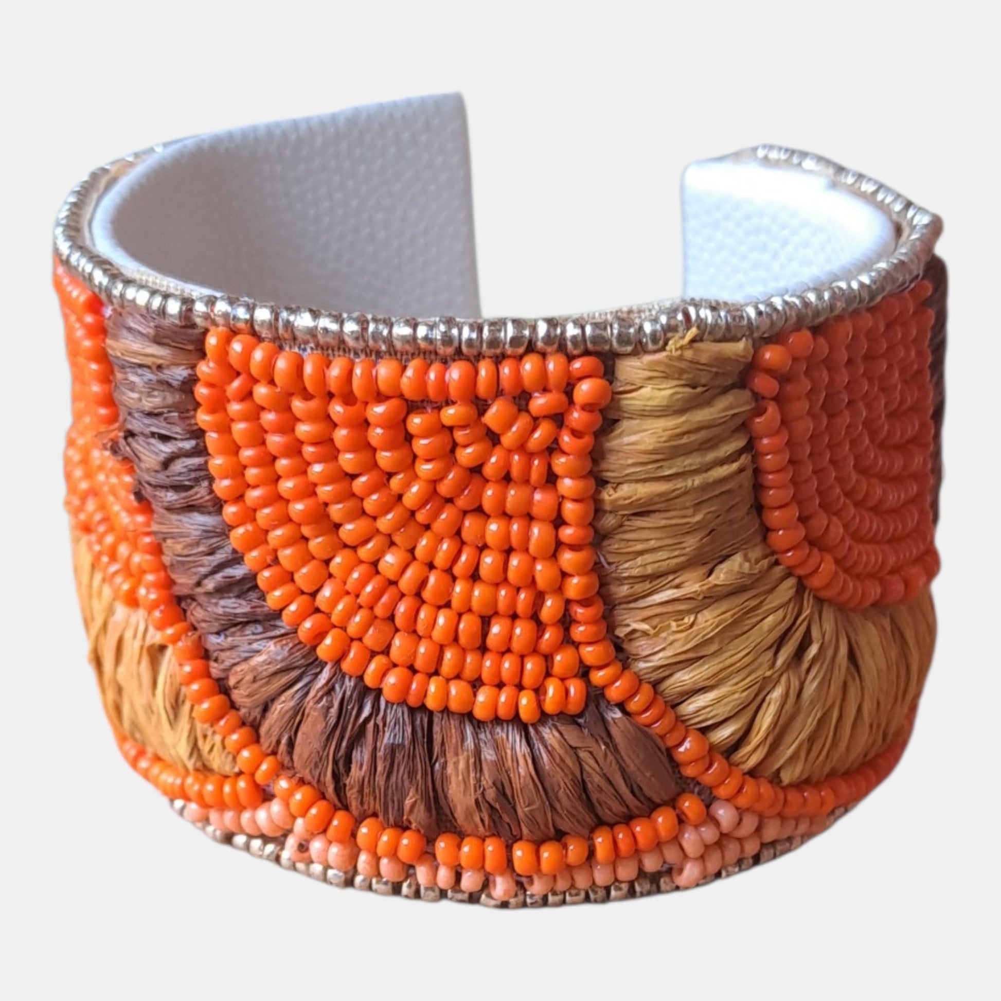 A wide cuff bracelet featuring geometric patterns of bright orange, brown, and tan seed beads over a white textured inner lining, finished with silver-toned beaded trim, measurements: 4,5cm wide, 18cm circumference