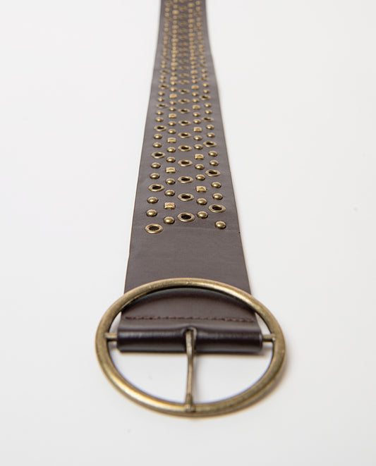 Wide brown belt in smooth faux leather, covered in studs and metal eyelets with an aged finish, and a round buckle. 104cm long, 6.5cm wide