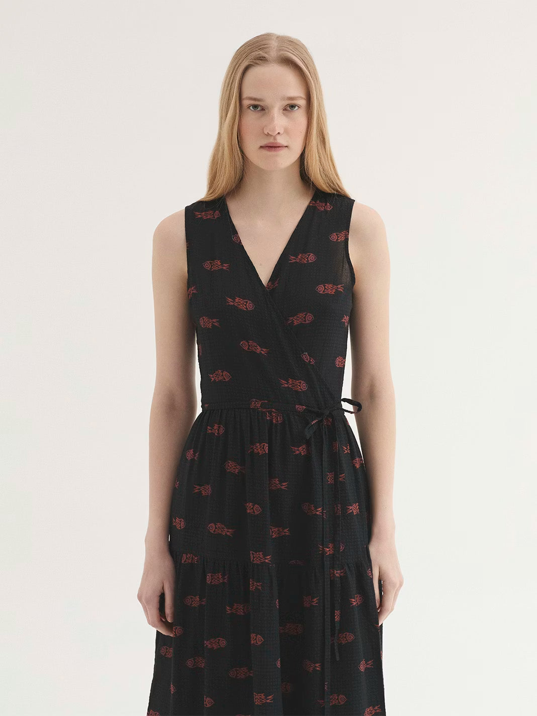 Mesh-knit fabric black dress with Ithaca Fish print, in orange and mauve colors, wrap dress with self-fabric tie waist, V neck, natural waist, ruffle skirt and side pockets.