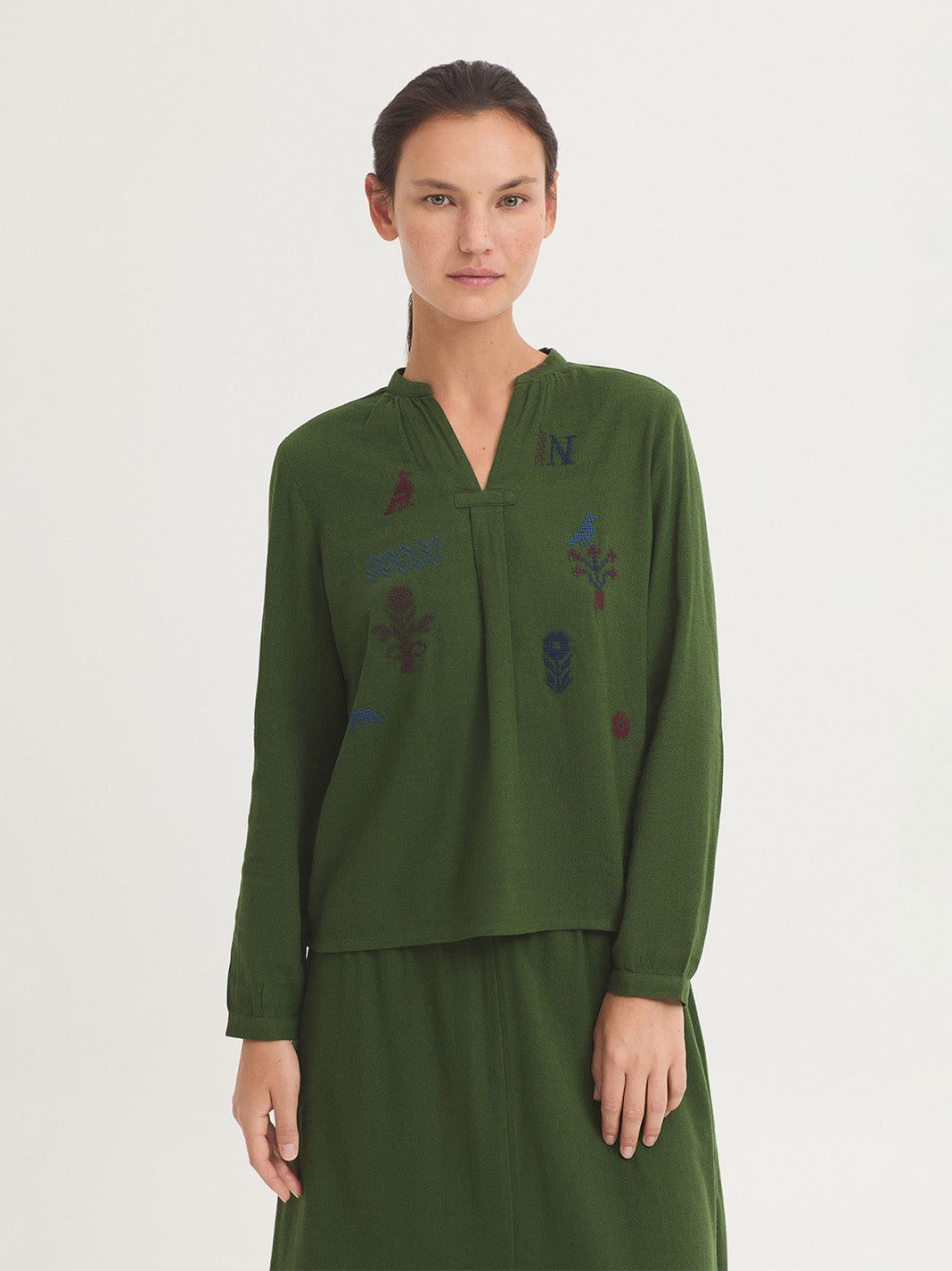 Blouse green in sustainable cotton blend fabric, Mao collar with opening, cross stitch embroidery on the front in blue, bordeaux and red colors,  puff sleeves with cuff and button, 60% Cotton, 40% Viscose.