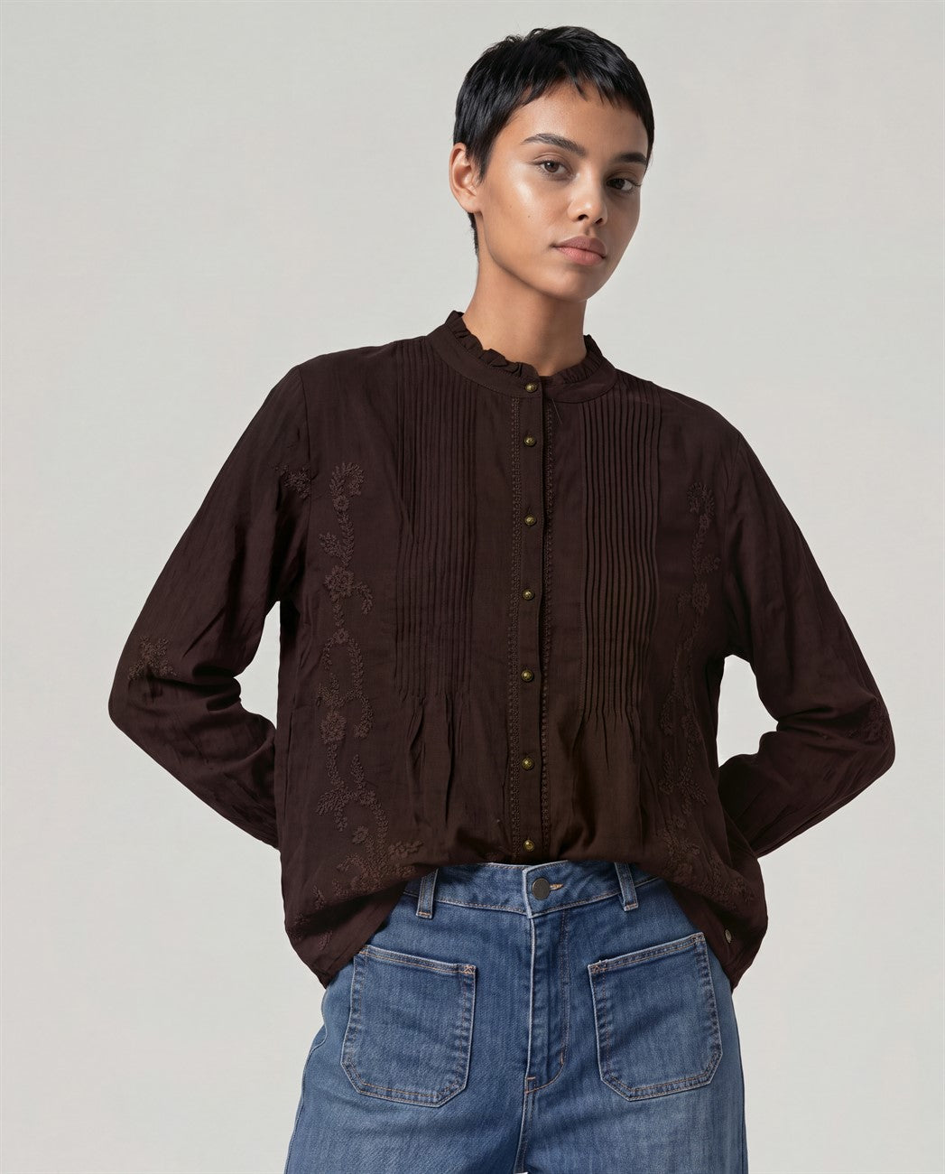 Shirt chocolate in soft viscose with front fine pleats and a ruffled mandarin collar. Same color embroidery across the body, metal buttons and ruffled cuffs for a light, romantic long-sleeve drape.
