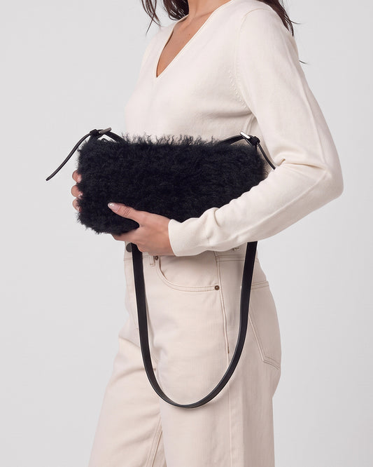 Baguette black bag in long-pile faux fur with a plush feel. Small, elongated shape with a thin adjustable strap and zip closure, 28cm x 16cm x 7cm