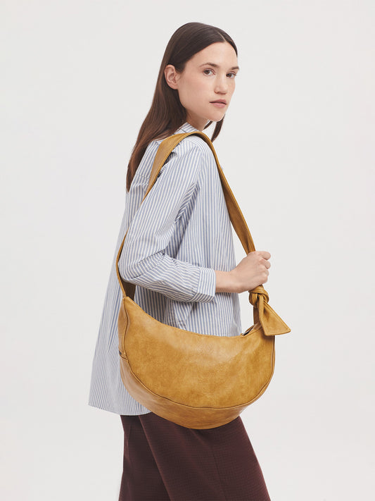 Half moon bag finished in soft washed dark yellow faux leather, adjustable strap with knot detailing, zip top fastening and side zipped pocket. Debossed logo and inside pockets.