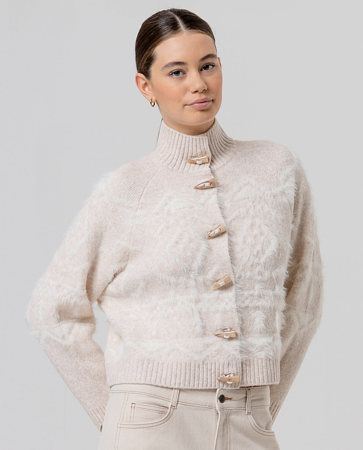 Ecru high funnel-neck cardigan with decorative buttons, in soft, warm knit with cotton. Raised jacquard in soft beige pile with a plush texture. Short and cosy.