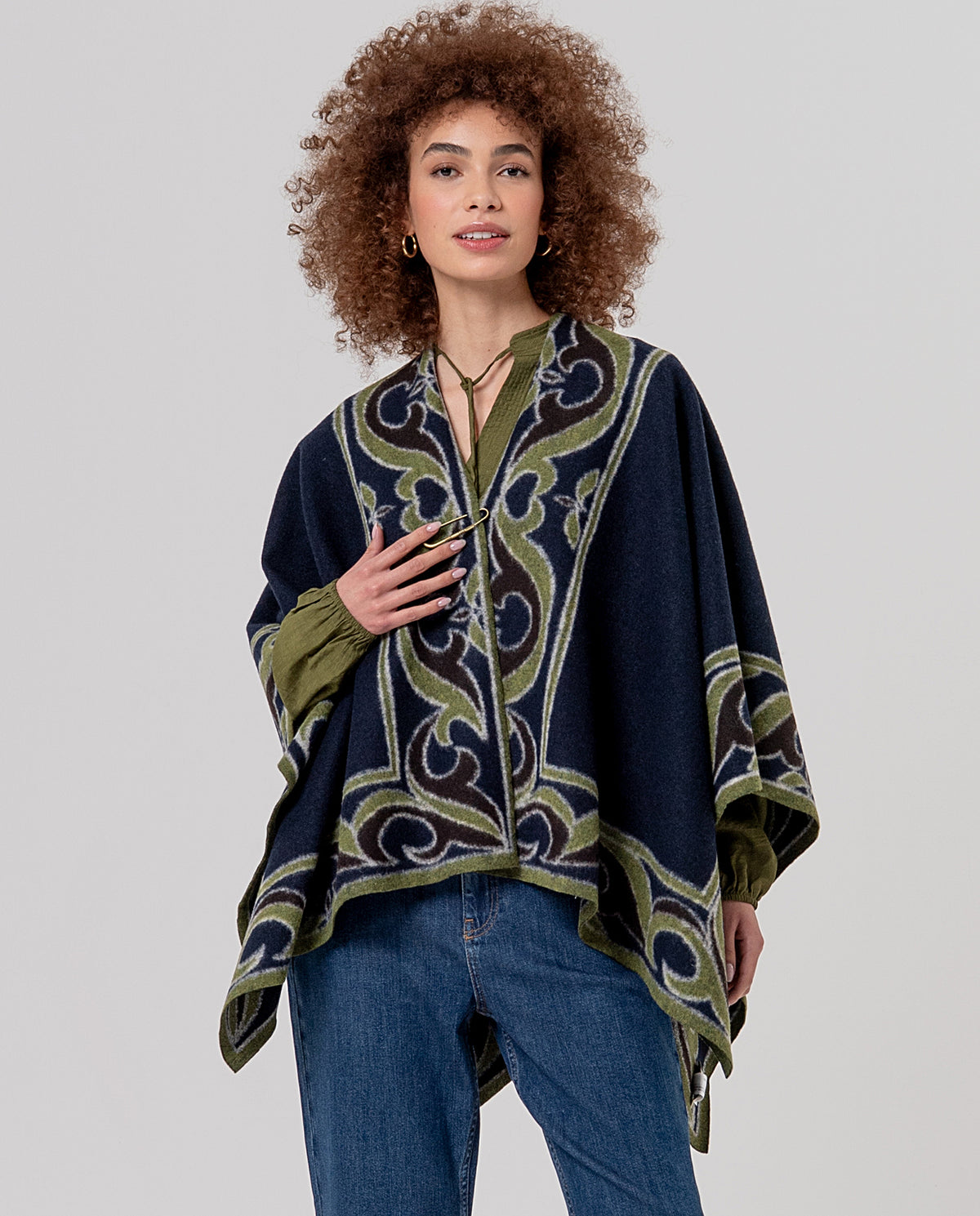 Open cape-poncho in warm knit with a pin fastening and contrasting trim. Wave and abstract jacquard in navy, khaki and purple colors with a felted texture.
