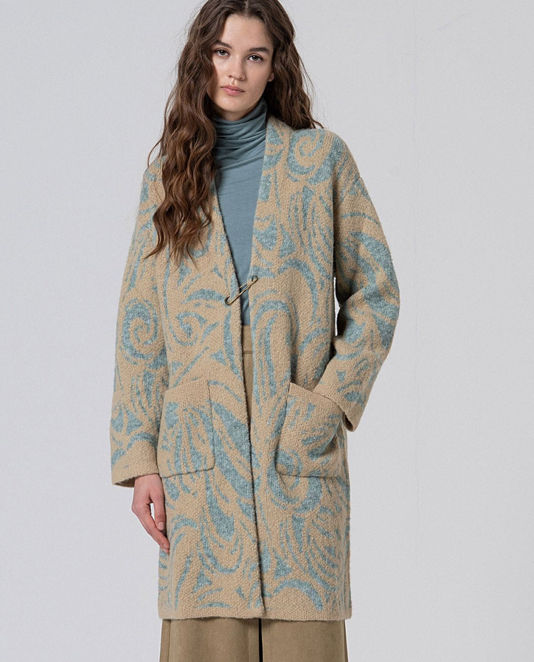 Long chunky knit coat with swirl light blue and beige jaquard print, with decorative buckle closure,  patch pockets and a kimono-like structure, in 50% Polyester, 30% Wool, 20% Recycled Polyester.