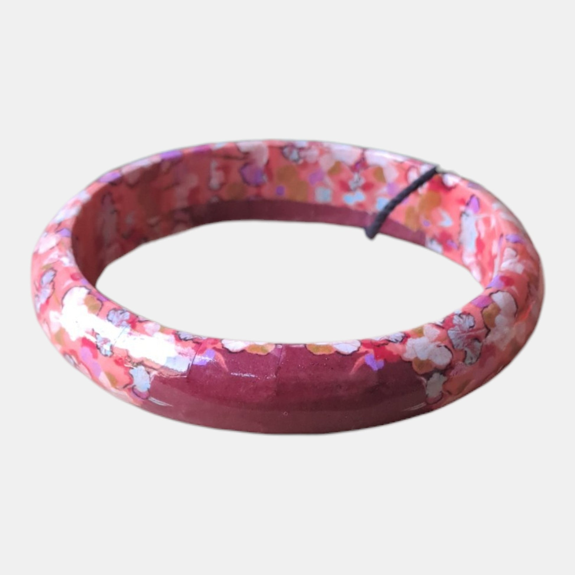 A circular bangle bracelet with a glossy flower pattern of pink, red, orange, and white
