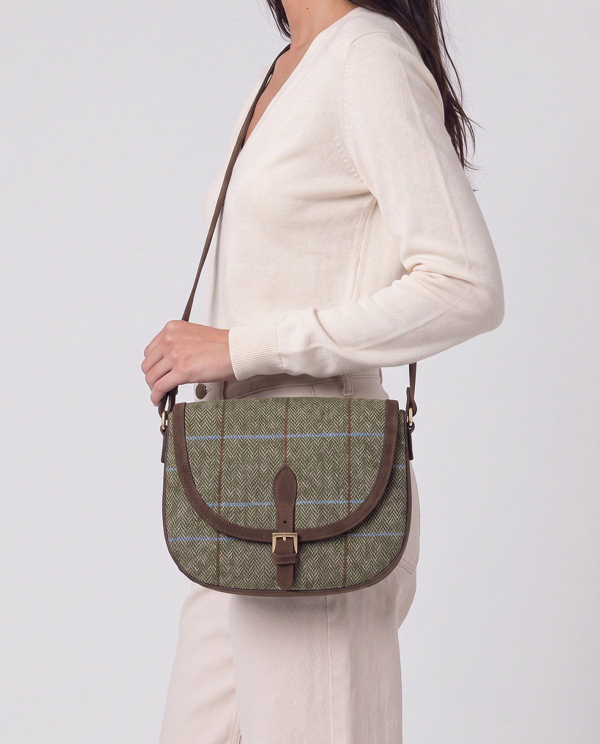 Saddle-style crossbody bag with a curved flap and buckle closure. Body in warm, textured green wool check fabric, with brown suede-effect trims. Adjustable strap. Inner open pocket and zip pocket, 26cm x 20cm x 2,5cm