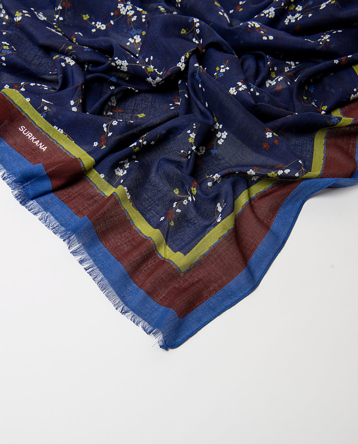 Rectangular navy scarf in light viscose with fluid drape. Delicate ditsy floral print of scattered sprigs in white, brown, light blue and light green colors, with a bright banded border and fringed trim.