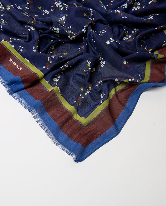 Rectangular navy scarf in light viscose with fluid drape. Delicate ditsy floral print of scattered sprigs in white, brown, light blue and light green colors, with a bright banded border and fringed trim.