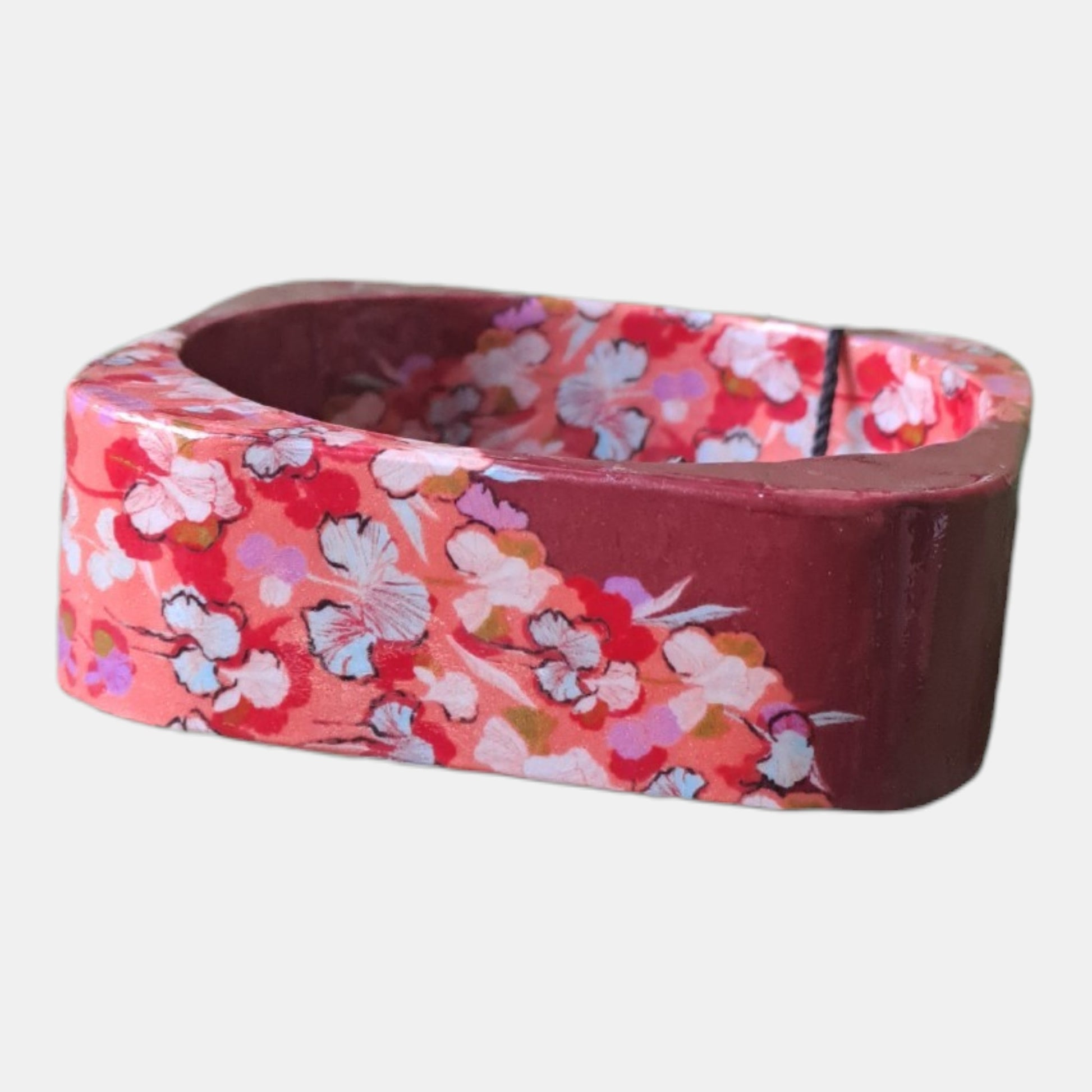 A handmade wooden bangle bracelet featuring a vibrant floral pattern on one side and a solid dark reddish-brown finish on the other, 2,5cm wide, 7,5cm diam.