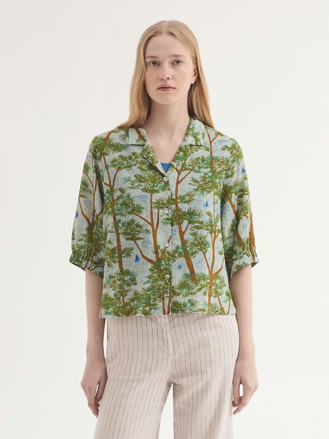 Pine Trees wood print shirt, ecru background color with blue like the sea and brown and green pine trees. notch lapels and button front, short sleeves with elasticated cuffs, in 50% Viscose, 50% Cotton