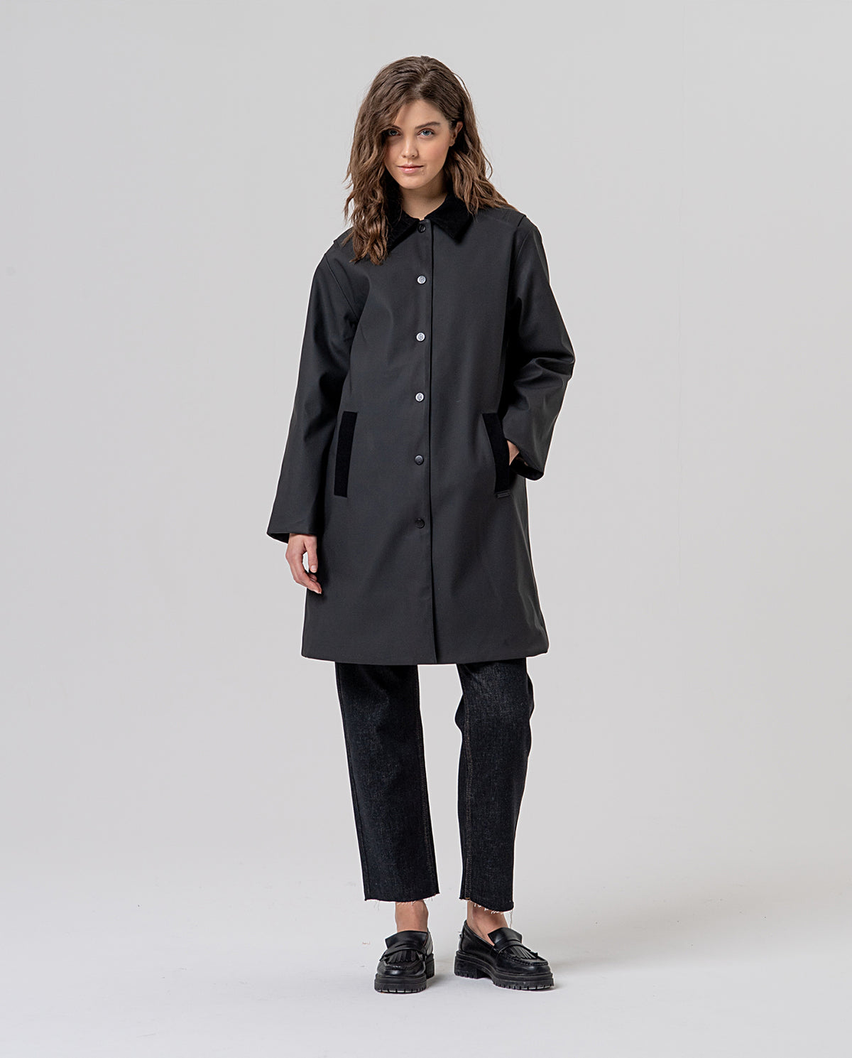 Straight black trench coat with a corduroy collar and front press buttons. Contrast-piped pockets and a checked inner lining. Roomy, clean silhouette, plain on the outside, for rainy days.