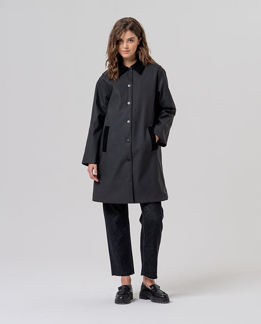 Straight black trench coat with a corduroy collar and front press buttons. Contrast-piped pockets and a checked inner lining. Roomy, clean silhouette, plain on the outside, for rainy days.