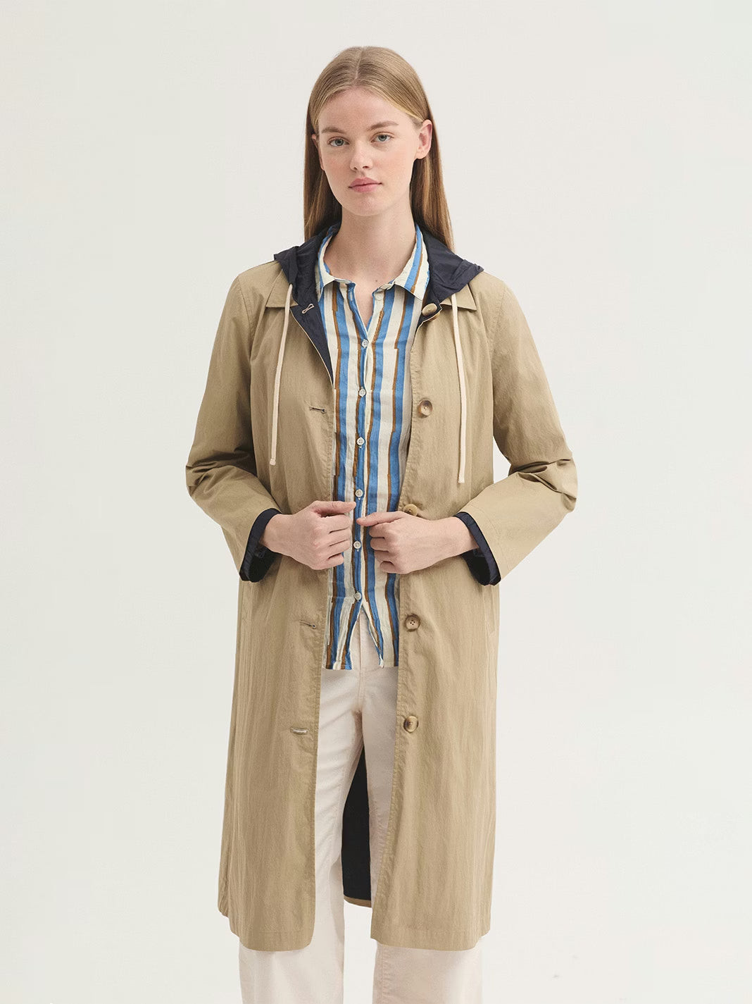 Reversible trench coat beige and navy. Outer shell in water-resistant cotton and nylon fabric with shirt collar, button front and piped pockets. Inner in 100% water-resistant nylon, with patch pockets, hood and elasticated cuffs.