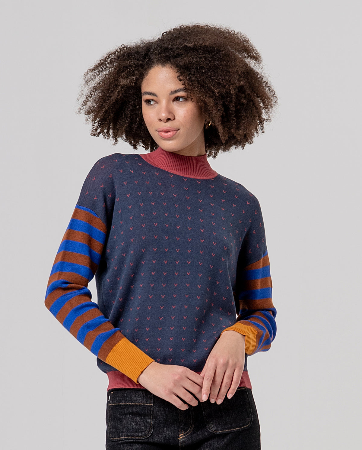 High-neck grey jumper in soft, fine knit. Body with a tiny polka-dot motif in terracotta color and striped sleeves in blue and mustard color, with terracotta cuffs and dark yellow trims in contrasting color