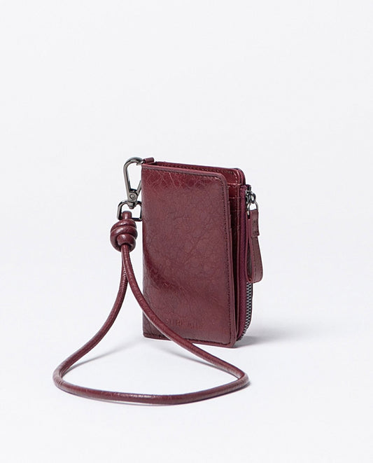 Compact wallet with crackle finish in bordeaux faux leather, includes compartments for cards, a zippered pocket and snap button closure, with removable strap handle.