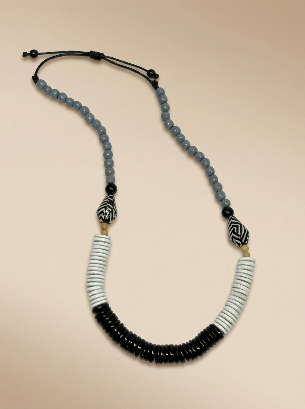 A beaded necklace featuring light blue-gray beads, black disc beads, white and black striped beads, and two black-and-white patterned accent beads