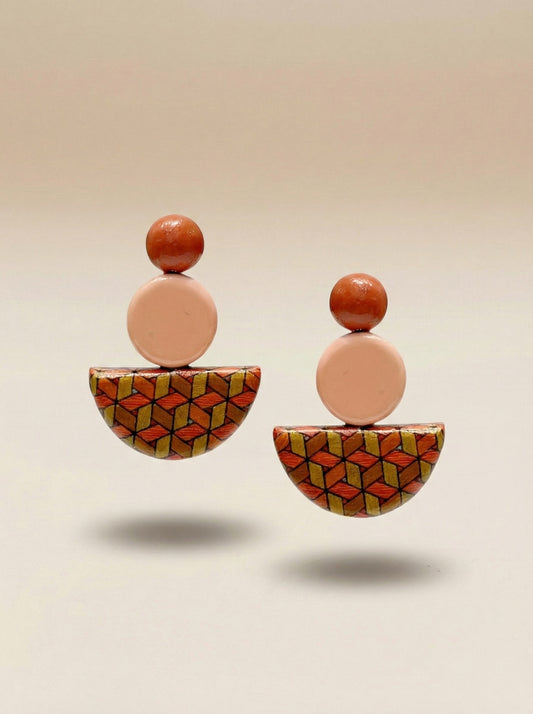 A pair of geometric drop earrings with peach-colored circular beads, small orange-brown spherical tops, and patterned semi-circular halves featuring orange, yellow, and black geometric designs