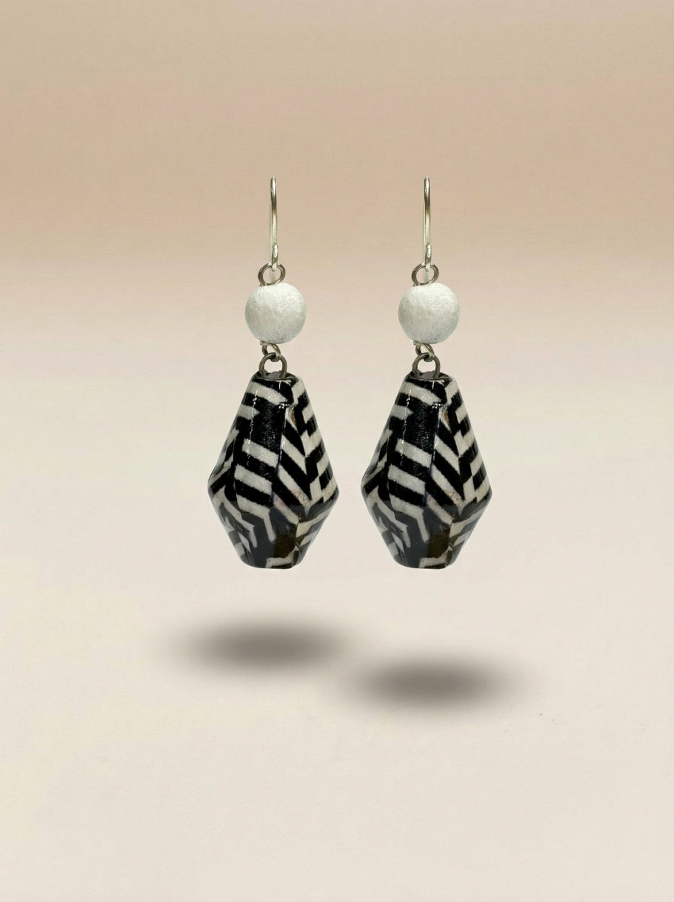 A pair of dangling earrings with white round beads and black-and-white patterned teardrop charms, from wood with brass hoks