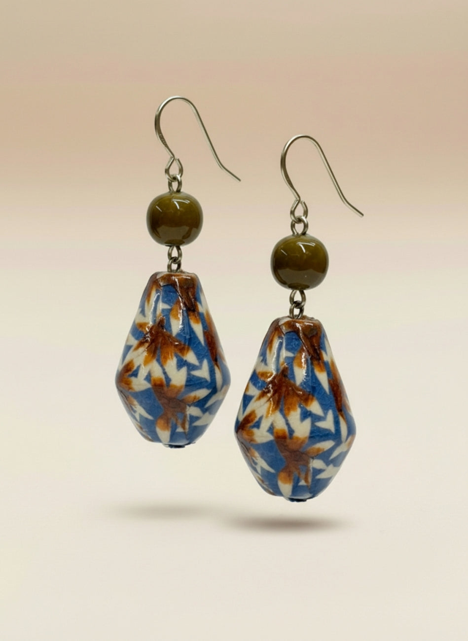 A pair of handmade drop earrings featuring teardrop-shaped beads with a blue, white, and brown floral pattern, accented by olive green beads and silver-tone French hook ear wires